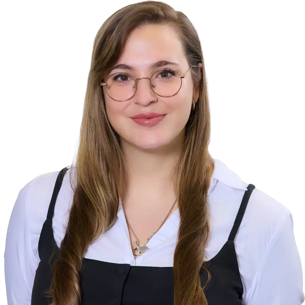Portrait of a young woman with round glasses, long light-brown hair, wearing a white shirt and black apron, smiling.